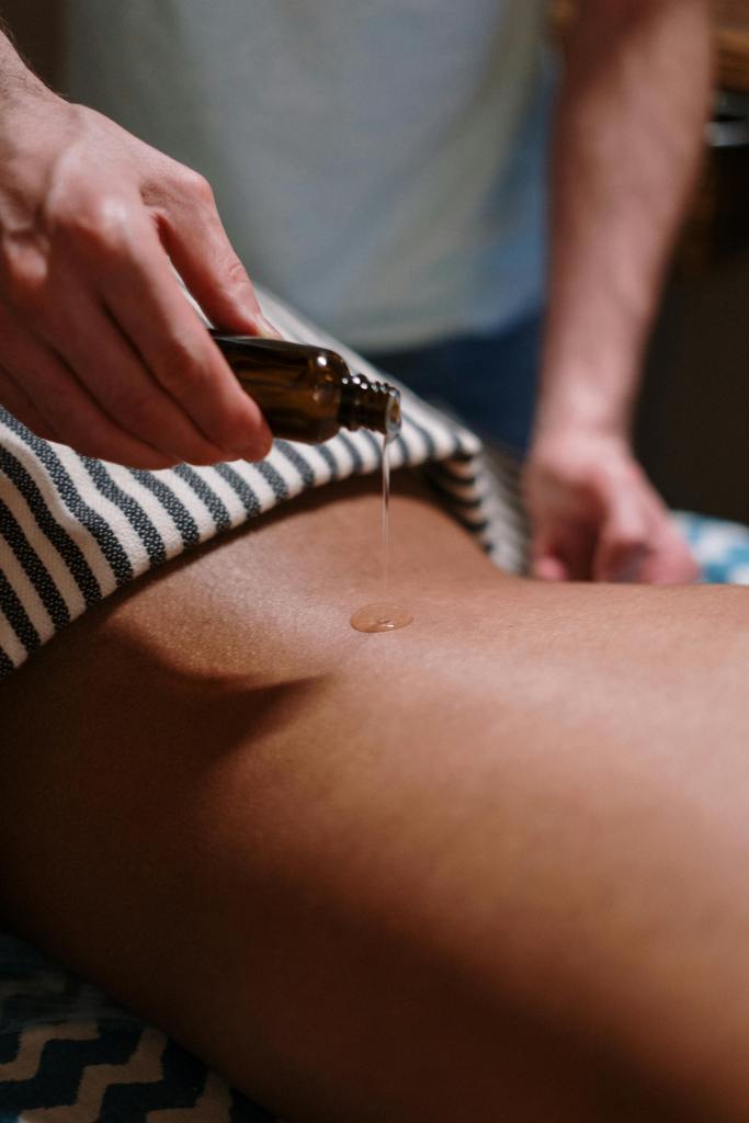 En terapeut som häller olja på en klädd person under en massagebehandling.